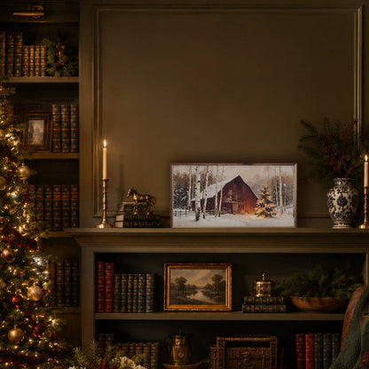Framed winter barn canvas print displayed on a cozy library shelf with Christmas decor