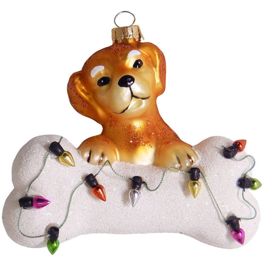 Glass Christmas ornament golden puppy resting on glittery white bone with colorful lights