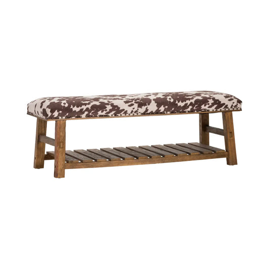 Upholstered bench with brown and white cowhide print cushion and rustic wood frame with slatted shelf