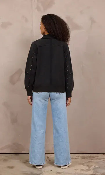 Black studded quarter-zip sweatshirt with embellished sleeves, worn with wide-leg jeans
