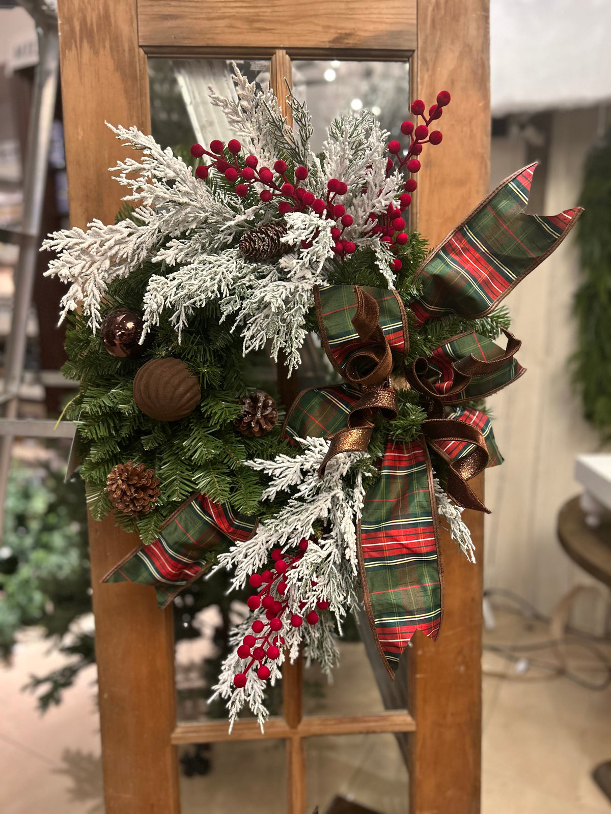 Frosted Christmas wreath with red berries, plaid ribbon, pinecones, and brown ornaments