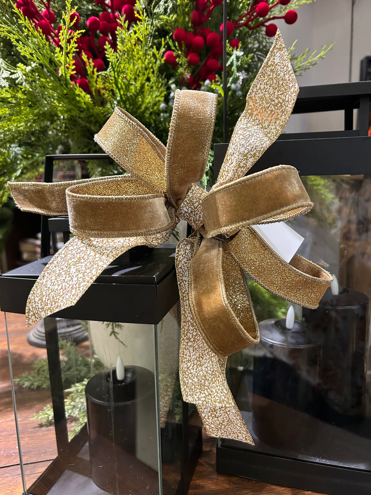 Elegant gold shimmer wired ribbon bow on black lantern with holiday greenery