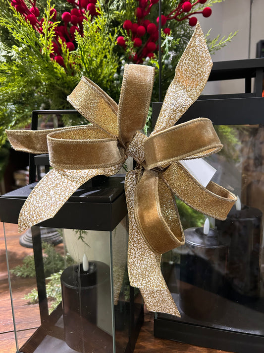 Elegant gold shimmer wired ribbon bow on black lantern with holiday greenery