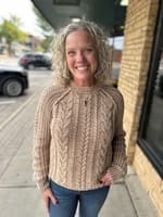Tan cable knit crew neck sweater with textured pattern worn with blue jeans