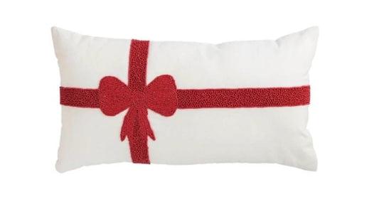 White lumbar pillow with red beaded ribbon and bow design by Mudpie