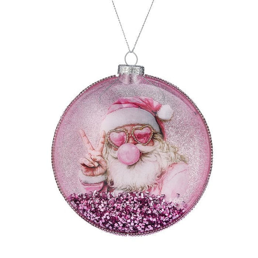 Round glass disk ornament featuring a pink-clad Santa with heart sunglasses blowing a bubble, filled with pink glitter