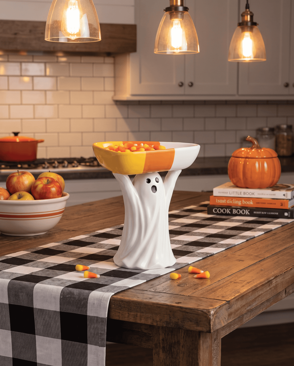 White ceramic ghost figurine holding a candy corn-colored bowl filled with candy corn, lifestyle kitchen setting
