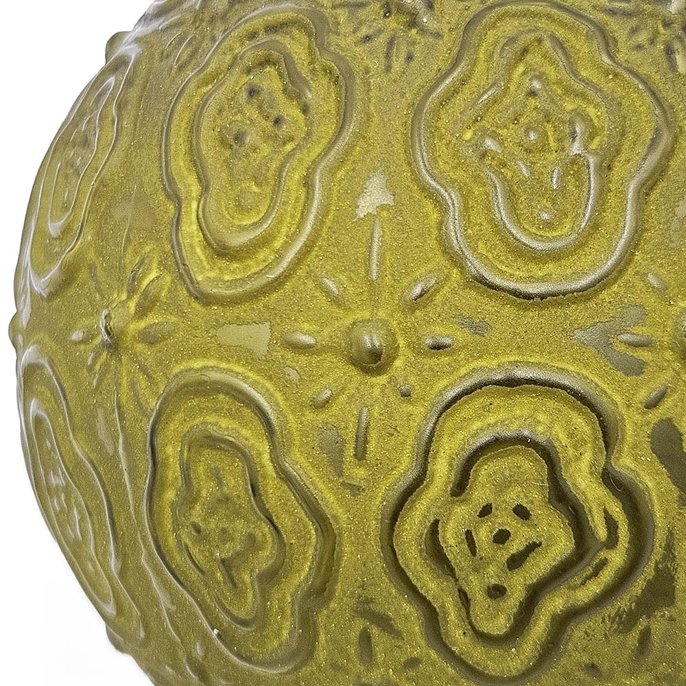 Close-up of a round ornament with embossed floral and swirl relief patterns in olive green glaze