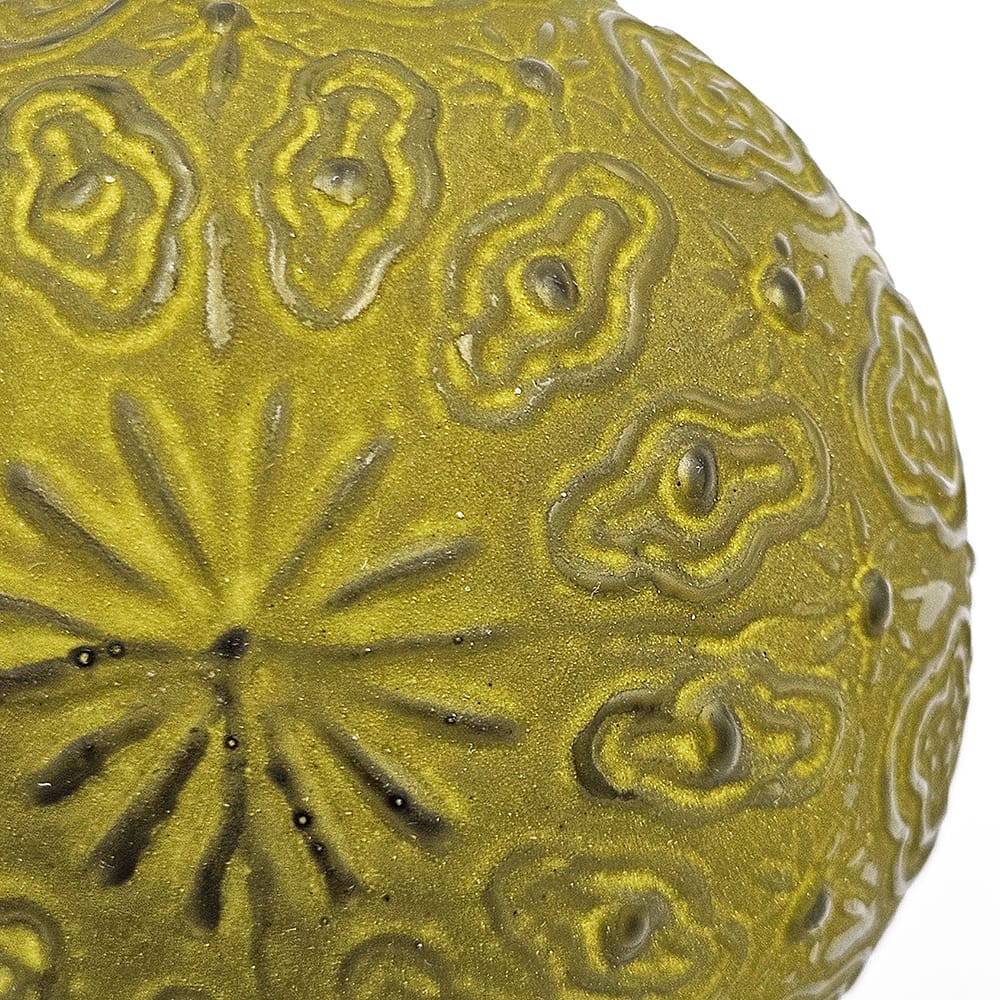 Close-up of a round ornament ball with embossed floral and scroll relief patterns in olive green