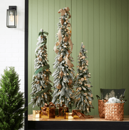 Flocked alpine Christmas trees with warm LED lights, ribbon, and gold ornaments