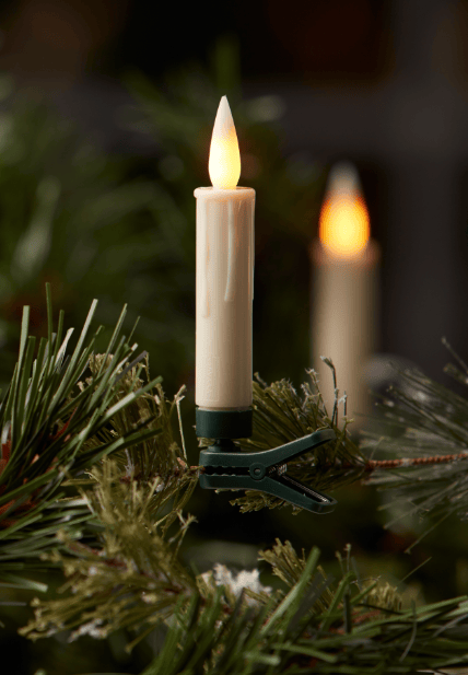 Cream LED clip-on candle with warm flame clipped to pine Christmas tree branch