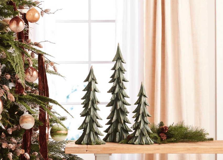 Set of three green rustic ceramic Christmas tree figurines in graduated heights on wooden surface