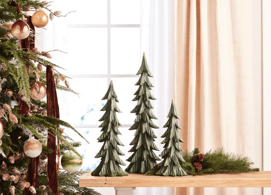Set of three green rustic ceramic Christmas tree figurines in graduated heights on wooden surface