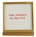 Gold metal frame with white insert displaying red text 'Lets conspire by the fire'