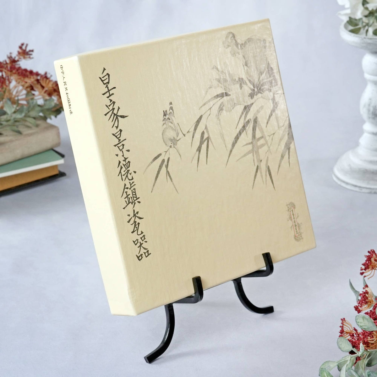 Black wrought iron easel displaying a cream Chinese art book with bamboo illustration