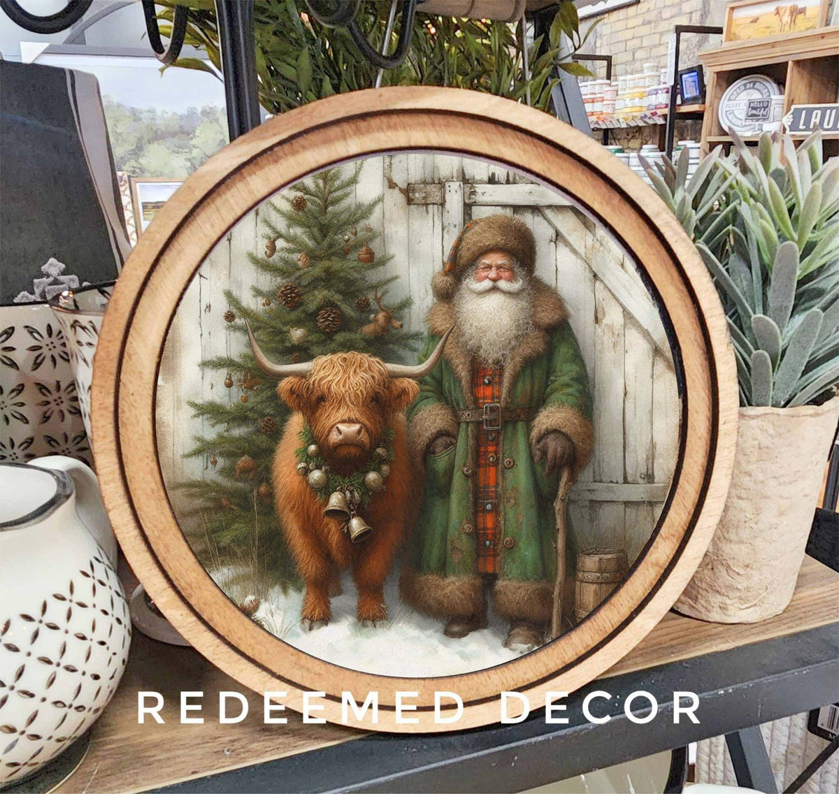 Round wood-framed sign with Highland cow and Santa Claus beside a Christmas tree