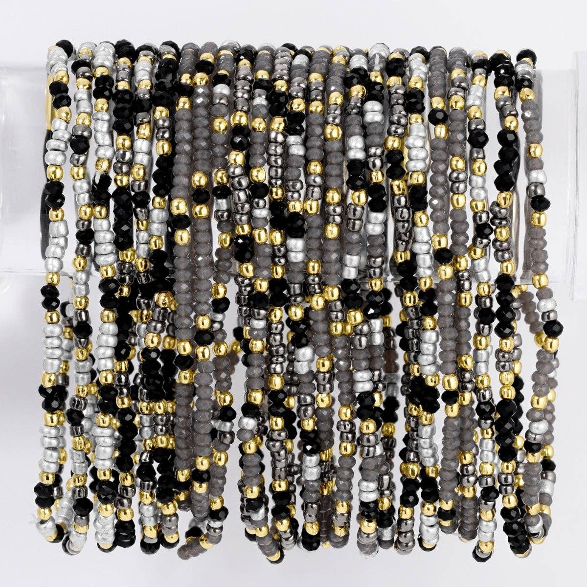 Stacked black, gray, silver, and gold seed bead stretch bracelets on display stand