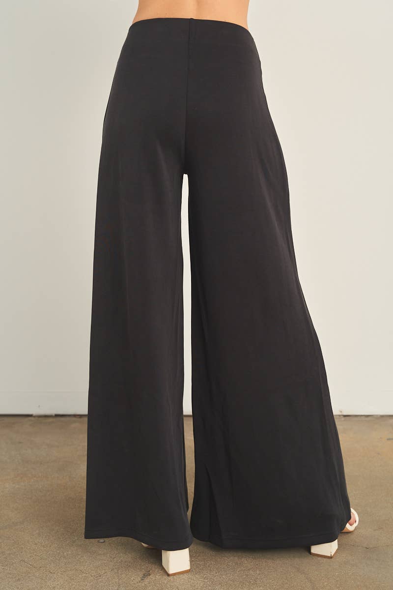 Black wide-leg palazzo pants with high waistband, back view, worn with white heels