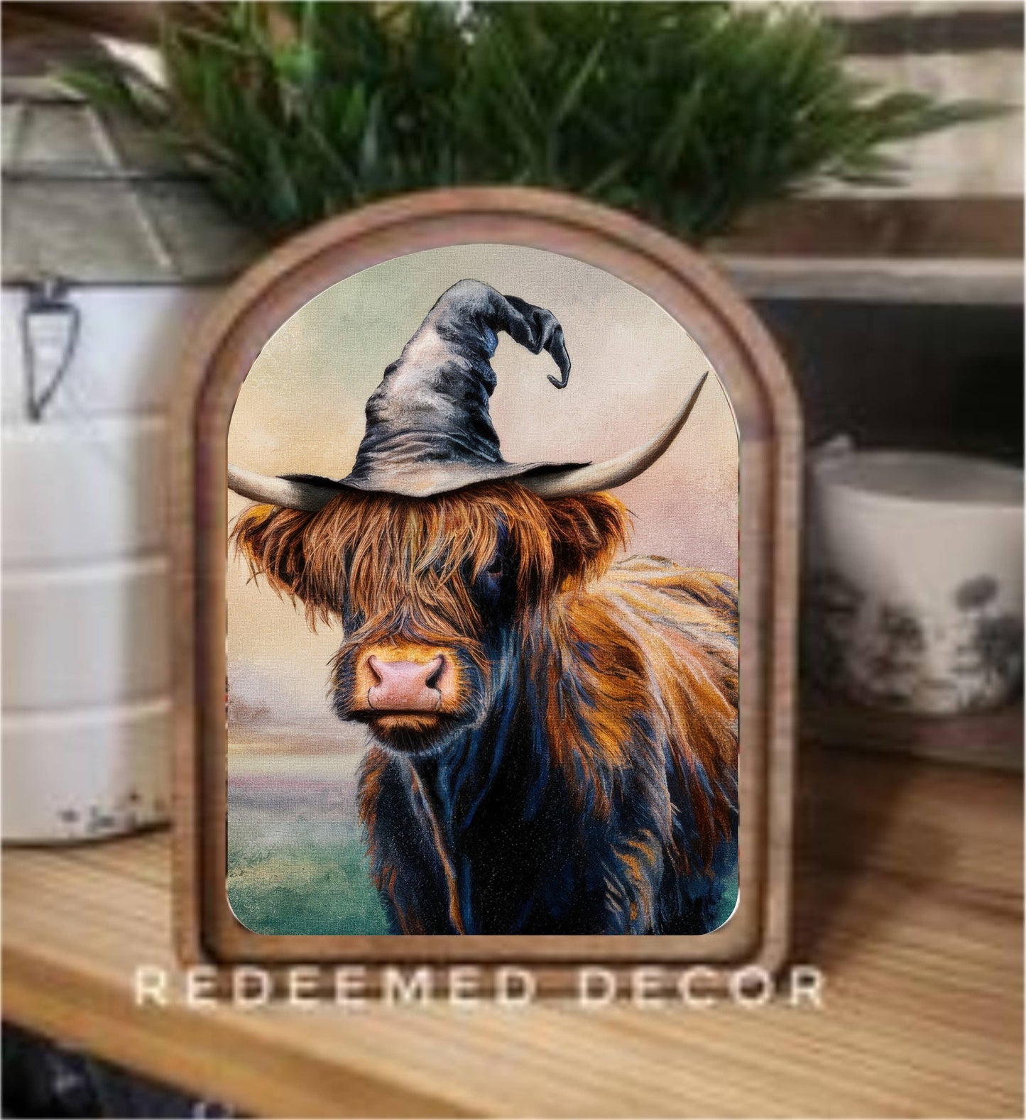 Arched wood-framed canvas art of a Highland cow wearing a witch hat