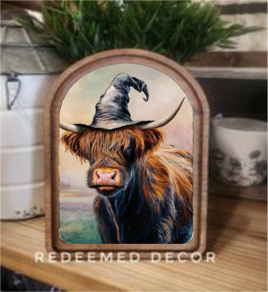 Arched wood-framed canvas art of a Highland cow wearing a witch hat