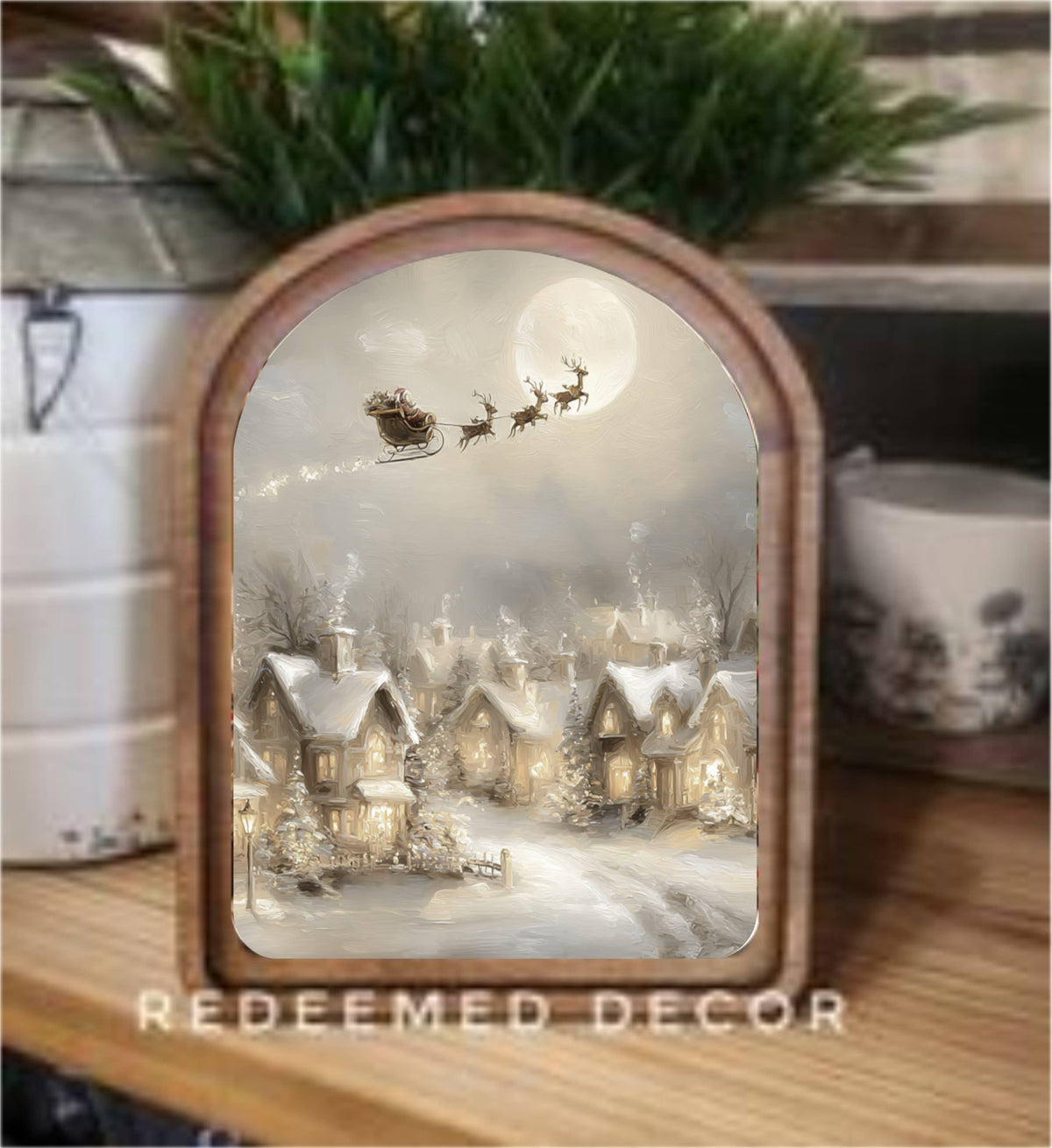 Arch-top framed canvas art depicting Santa's sleigh over a snowy village by moonlight