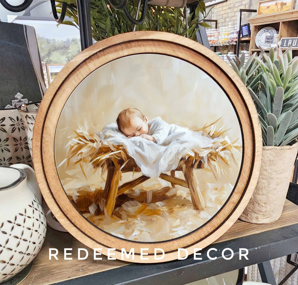 Round wood-framed canvas print of baby Jesus sleeping in a manger on hay