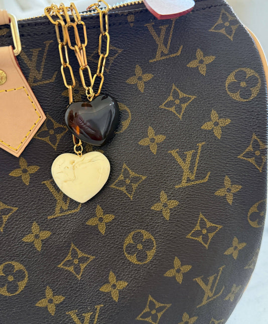 Gold paperclip chain necklace with dark brown and cream heart pendants on LV bag