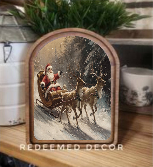 Arched wood-framed canvas art print of Santa Claus riding a reindeer sleigh in snow
