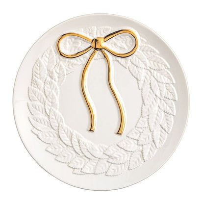 Round white ceramic plate with embossed leaf wreath and gold metallic bow detail, top view
