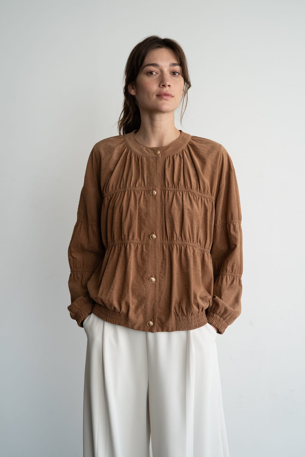 Women's tan suede blouson jacket with gold buttons, ruched detailing, and elastic hem