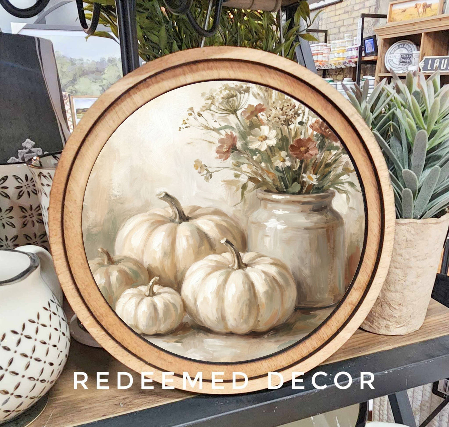 Round wood-framed canvas print of cream pumpkins and wildflowers in neutral tones