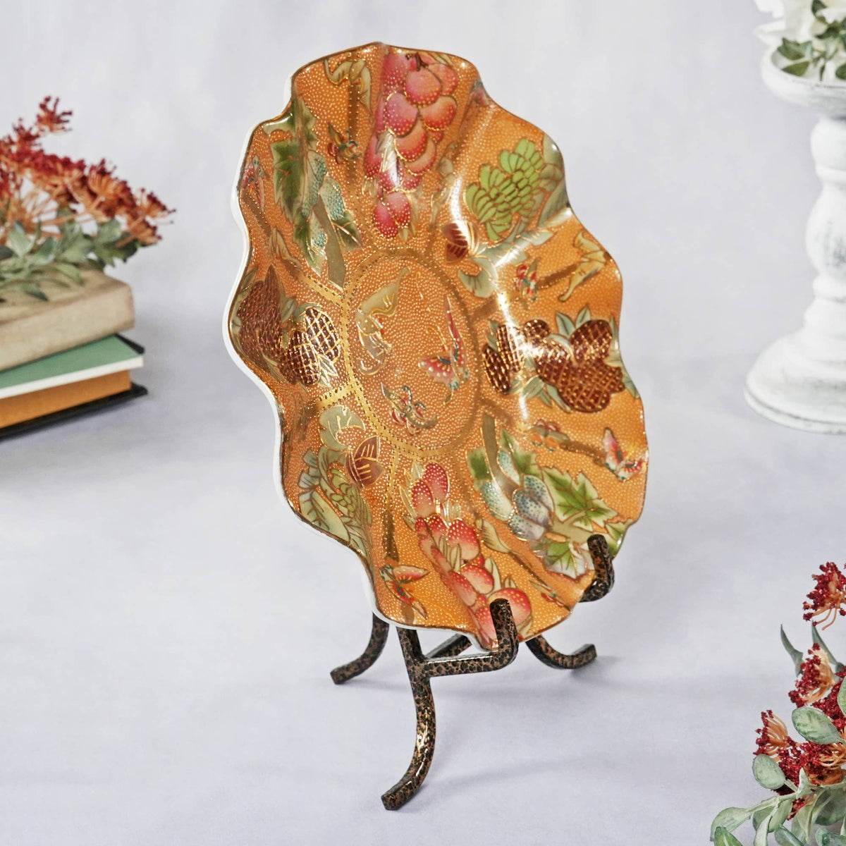 Wrought iron plate easel displaying ornate orange floral ceramic dish on white surface