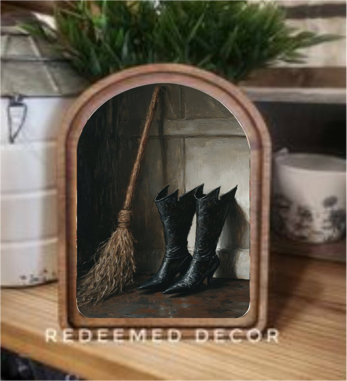 Arched wood-framed canvas art depicting black witch boots and a broom