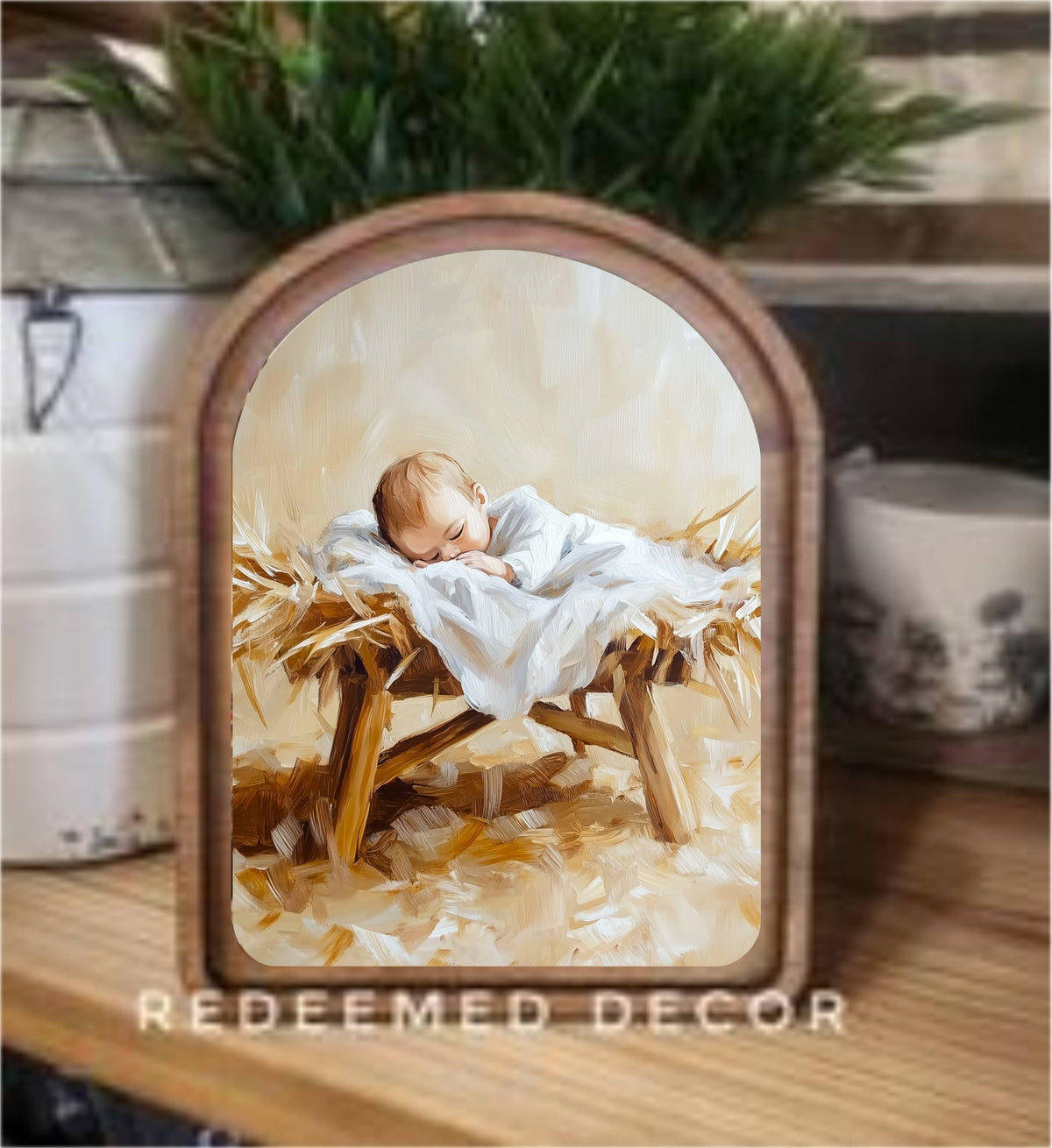 Arched wood-framed canvas art of Baby Jesus sleeping in a manger on hay