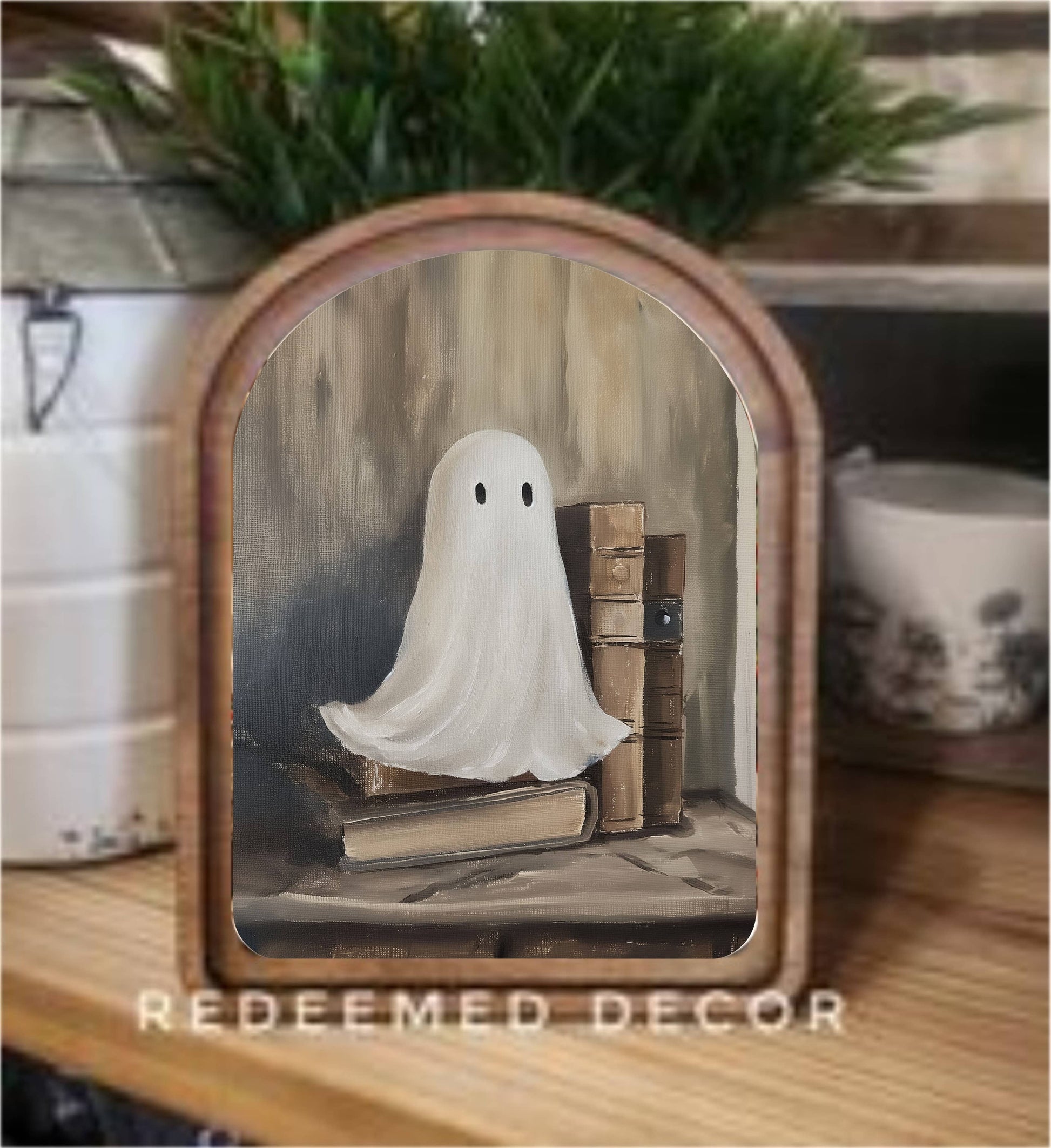 Framed arch-top canvas art of a white ghost sitting beside stacked vintage books