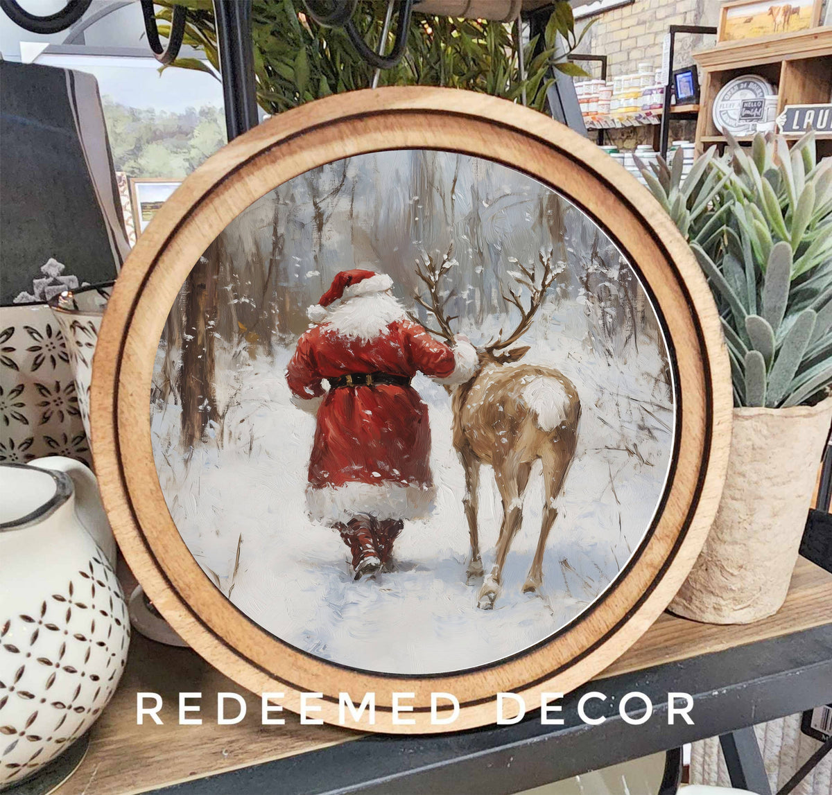 Round wood-framed canvas art of Santa and reindeer walking in snowy forest