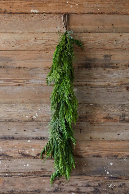 Long hanging evergreen garland bundle with cypress and pine sprigs on rustic wood wall