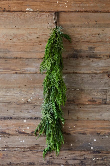 Long hanging evergreen garland bundle with cypress and pine sprigs on rustic wood wall