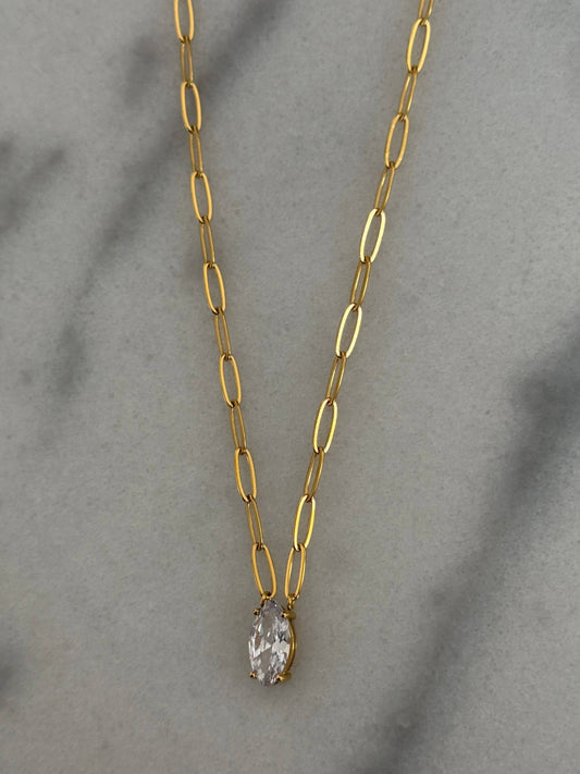 Gold paperclip chain necklace with pear-shaped clear crystal pendant on marble surface