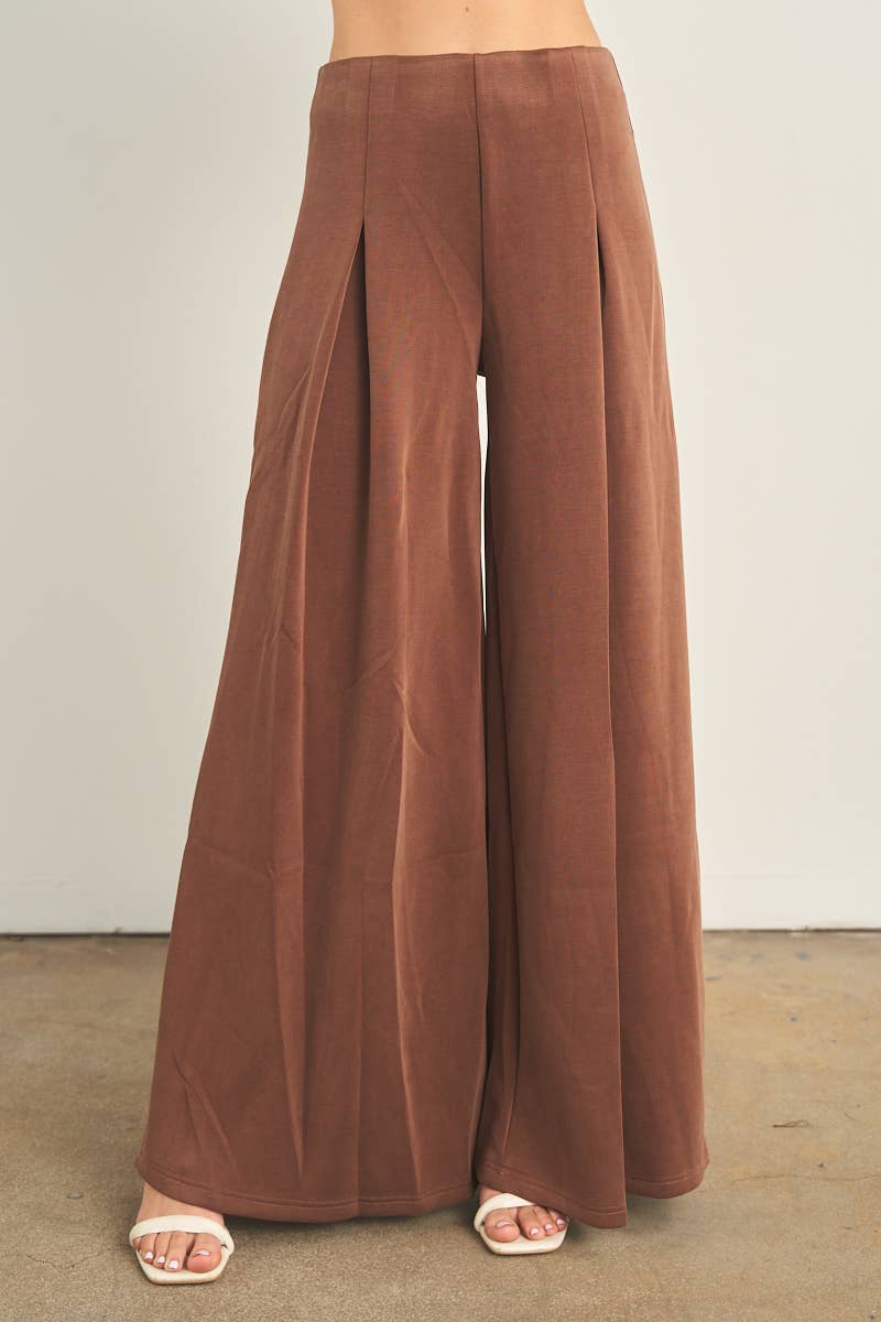 Brown wide-leg palazzo pants with pleats, worn with white heeled sandals