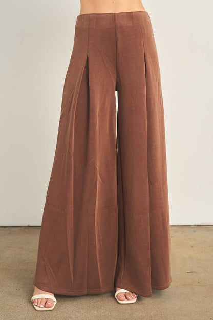 Brown wide-leg palazzo pants with pleats, worn with white heeled sandals