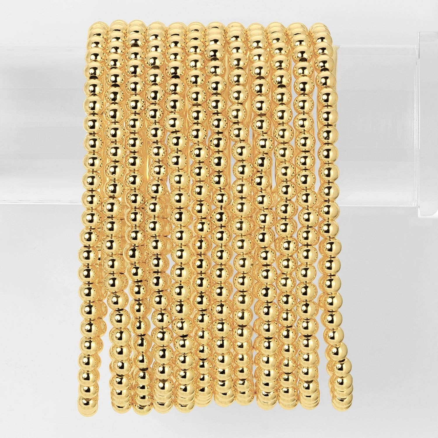 Stack of polished gold tone brass bead stretch bracelets displayed on clear acrylic stand