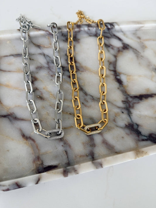 Silver and gold chunky paperclip chain necklaces with pavé crystal clasp links on marble tray