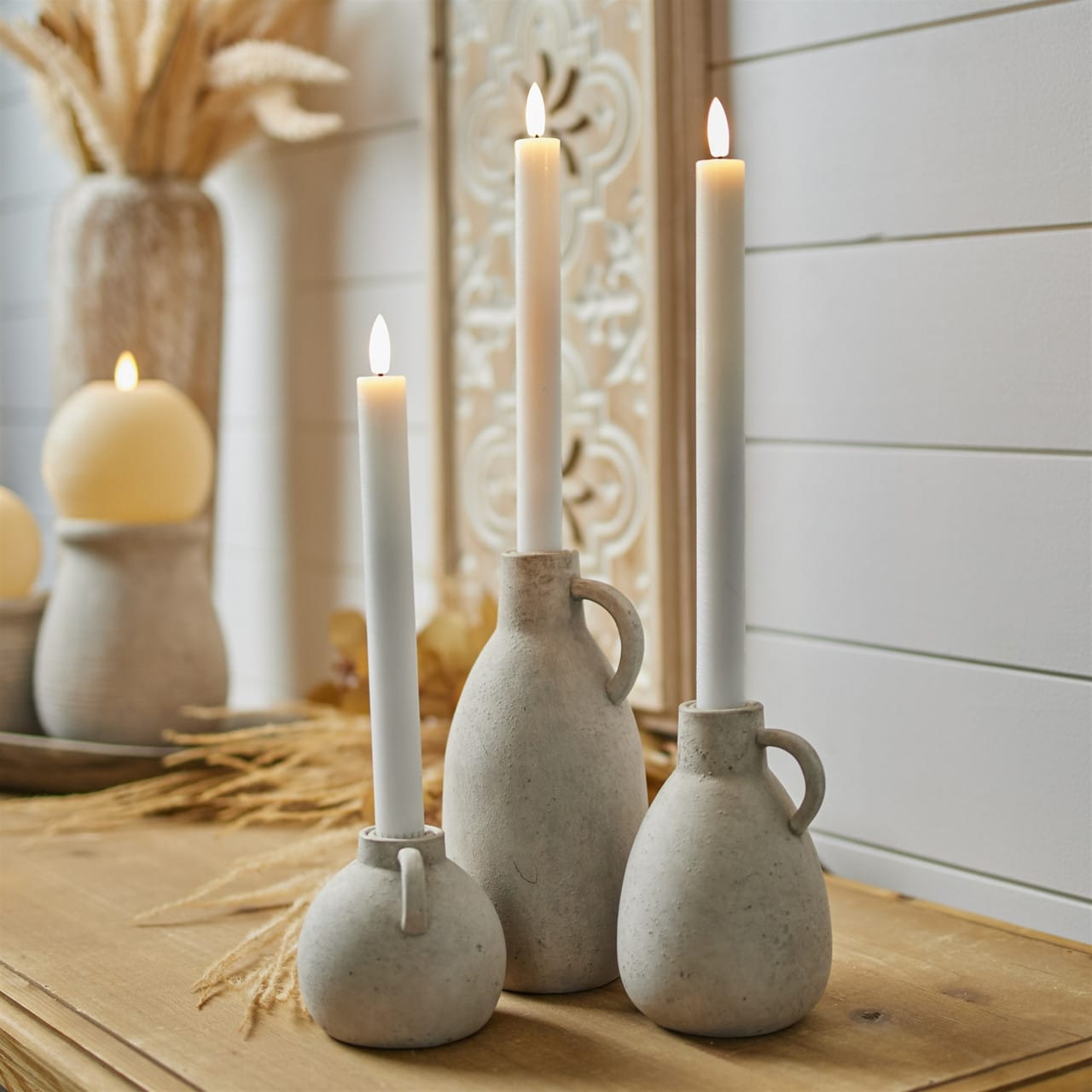 Ivory taper candles with lit flames displayed in rustic stone-textured ceramic jug holders