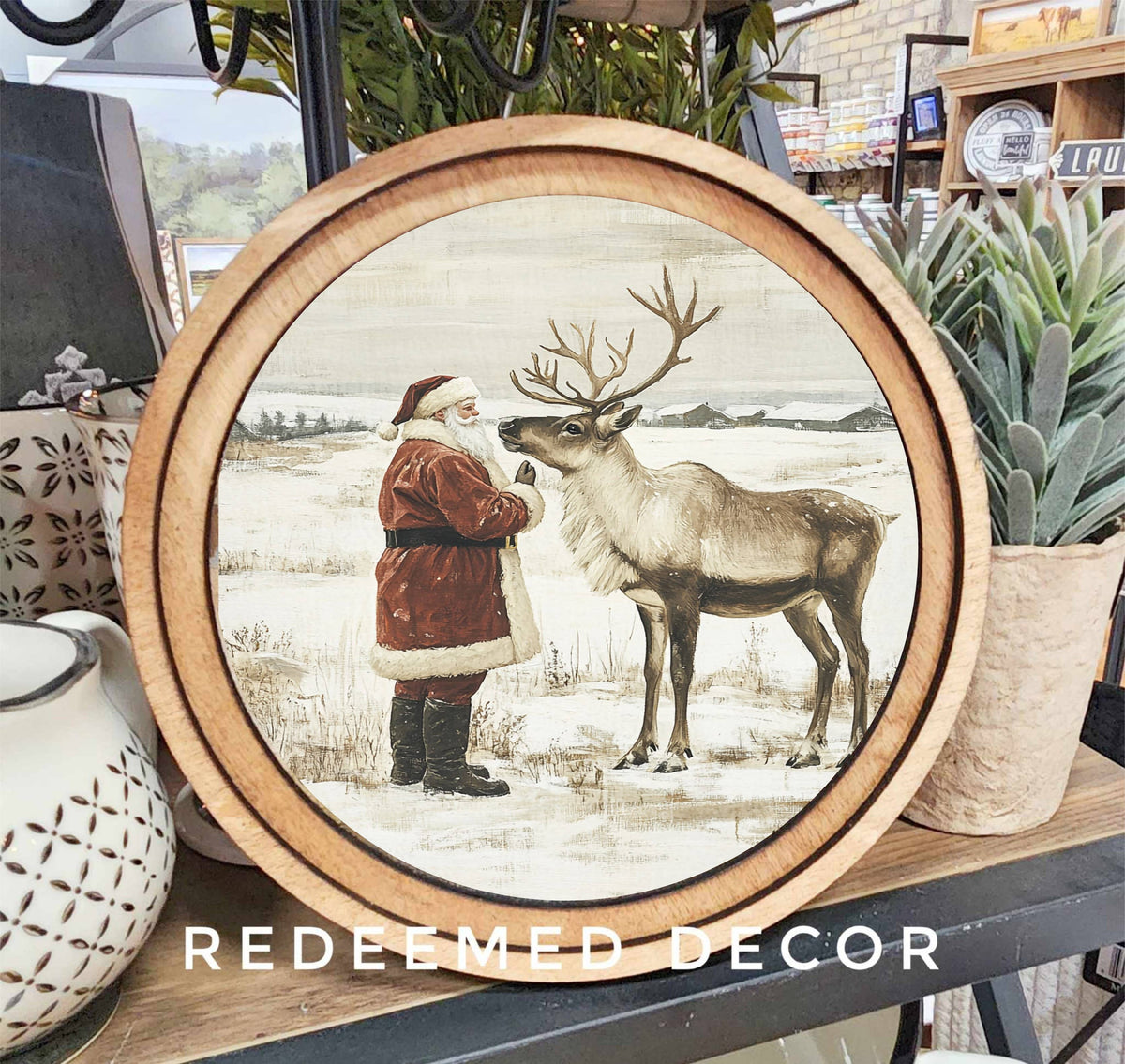 Round wood-framed canvas art featuring vintage Santa Claus feeding a reindeer in snow