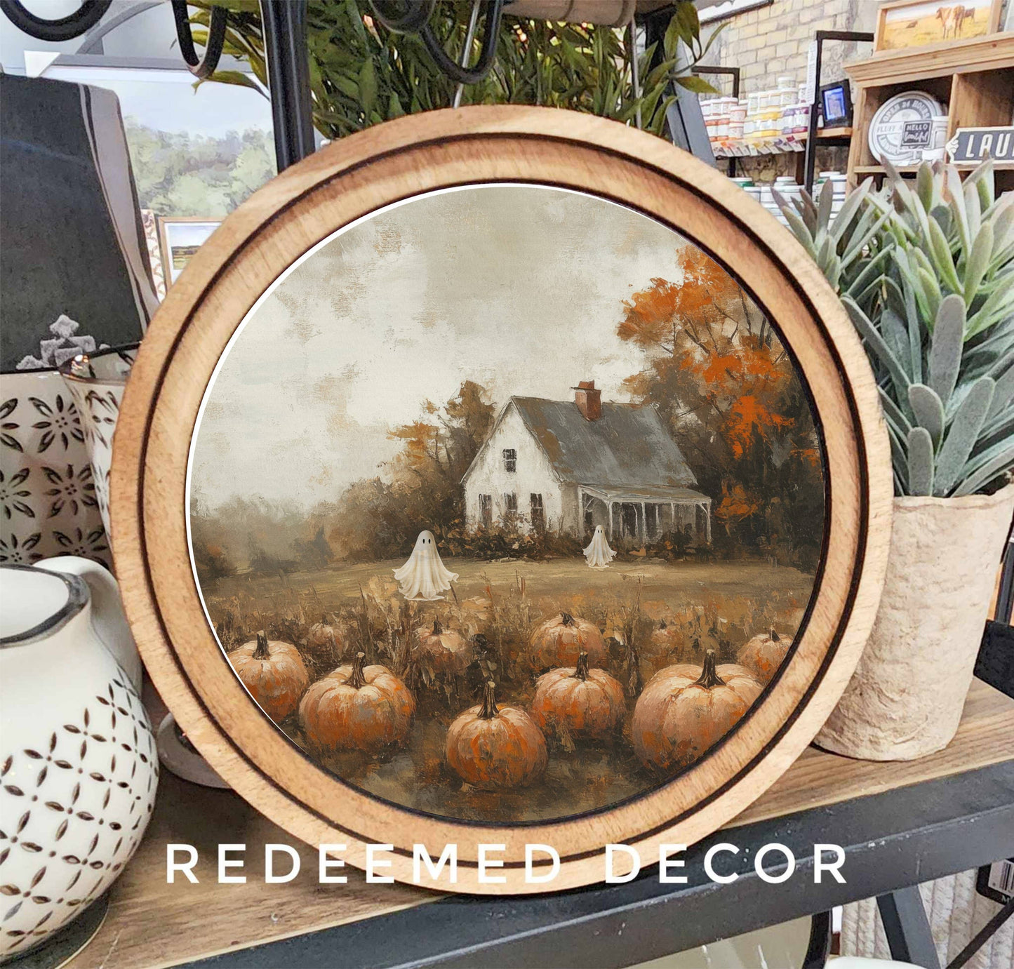Round wood-framed Halloween canvas art with pumpkin patch, ghosts, and farmhouse scene