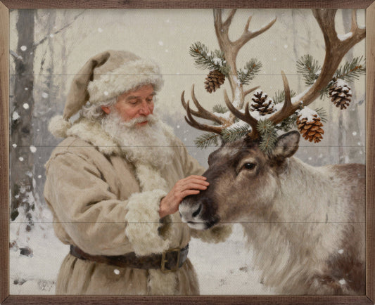 Framed oil painting of Santa in cream fur coat petting a decorated reindeer in snow