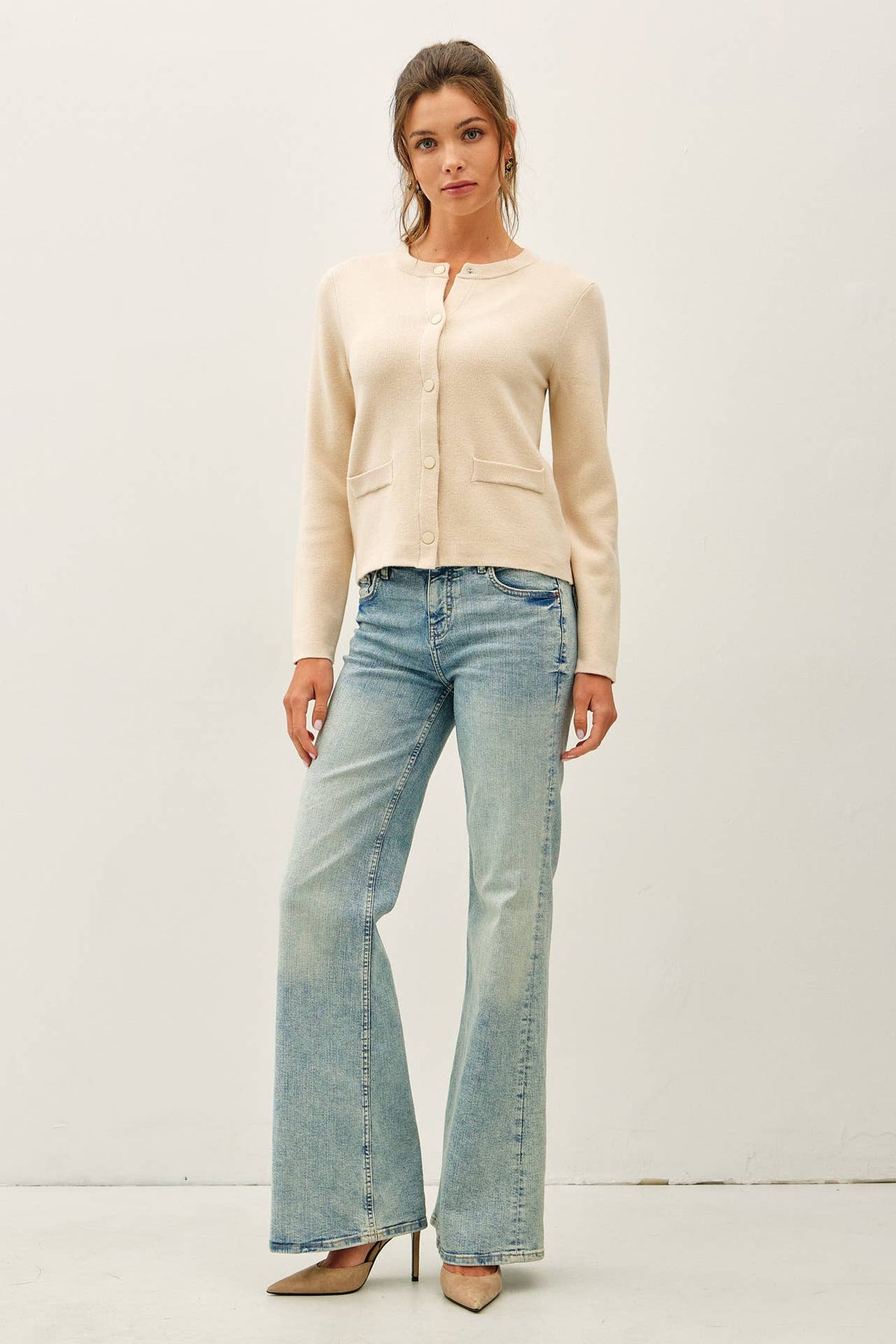 Cream crewneck cardigan with snap buttons and front patch pockets paired with flare jeans