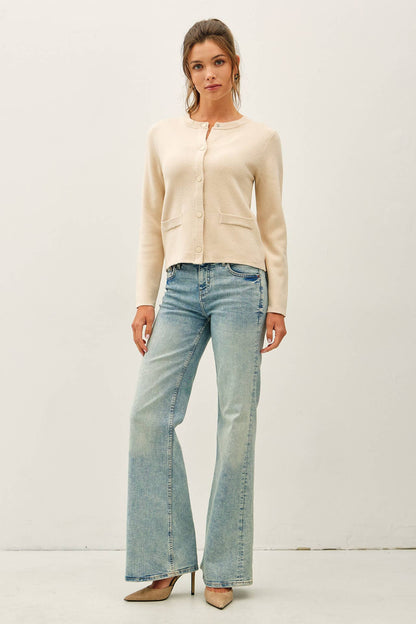 Cream crewneck cardigan with snap buttons and front patch pockets paired with flare jeans
