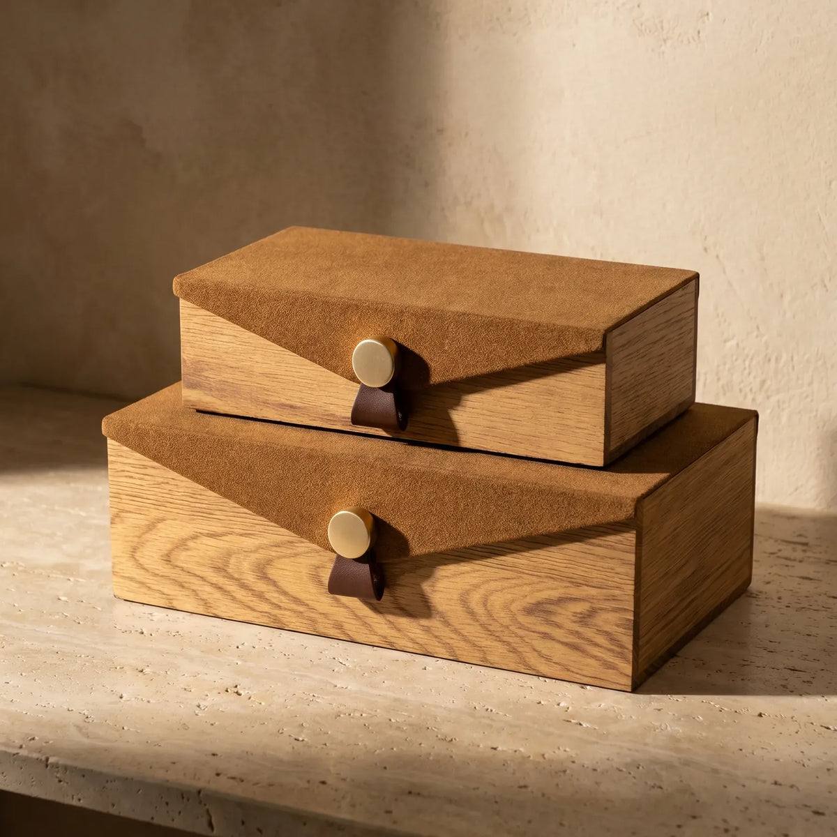 Two stacked oak wood storage boxes with tan suede lids and brass button closures